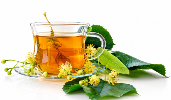A glass cup of herbal tea with linden blossoms and fresh green leaves