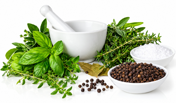 A white mortar and pestle with fresh basil and thyme, beside bowls of salt and black peppercorns